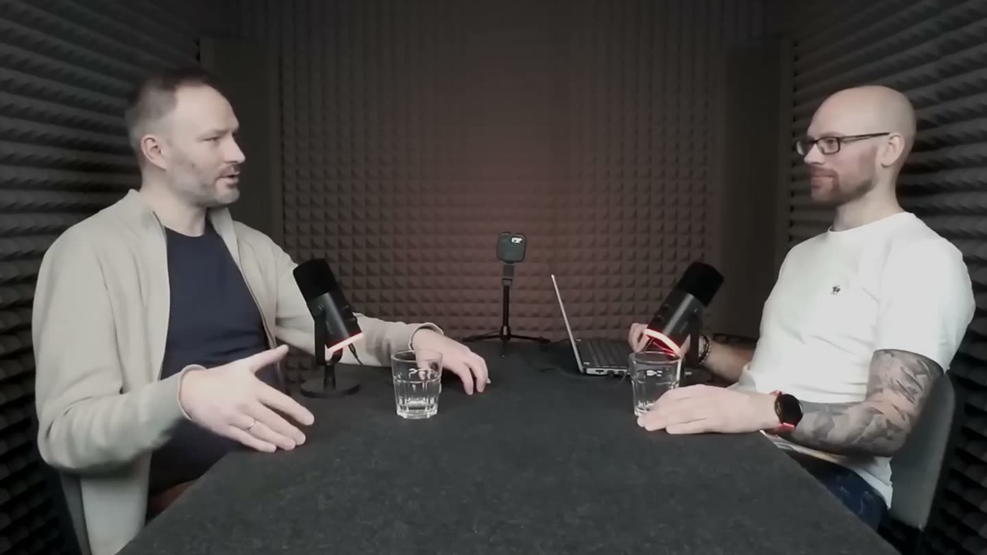 Marcin Sobczyk i Szymon Płodowski przy stole w wyciszonym studiu, przed nimi mikrofony i szklanki z wodą.